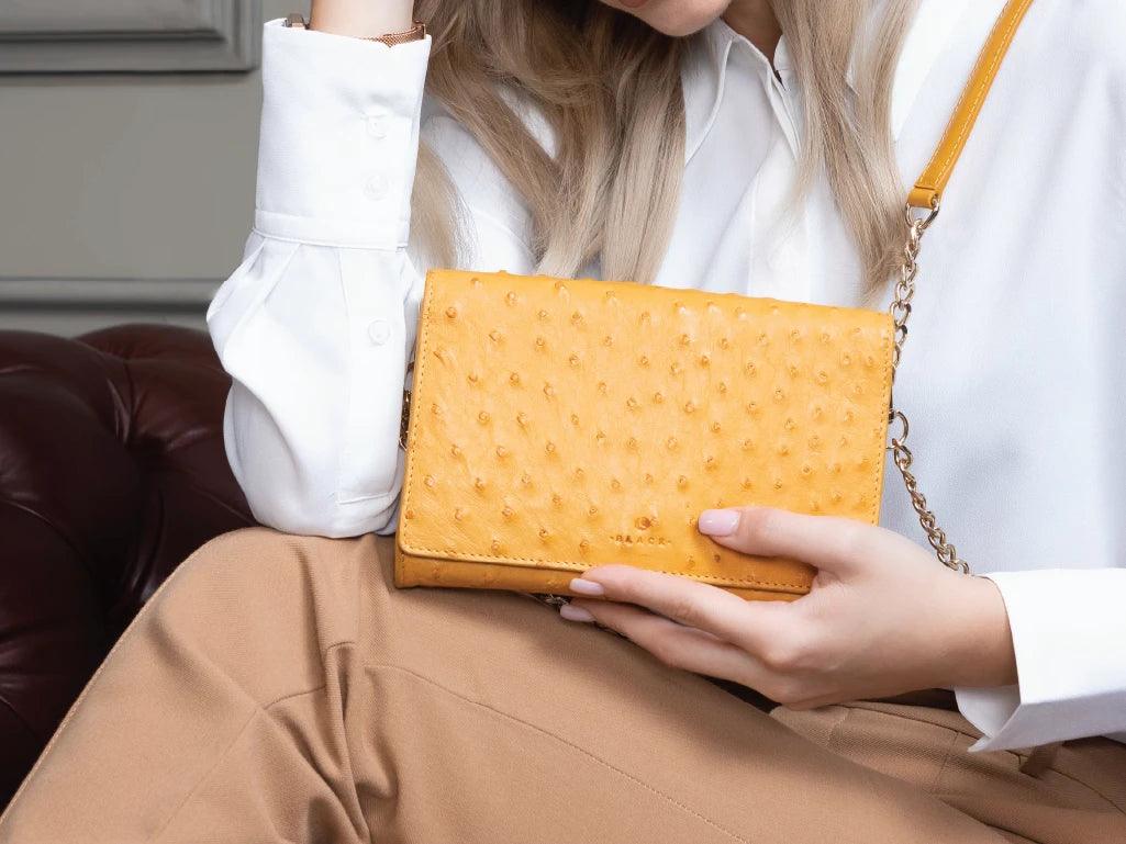 Woman holding yellow textured leather crossbody bag with gold chain strap, stylish accessories
