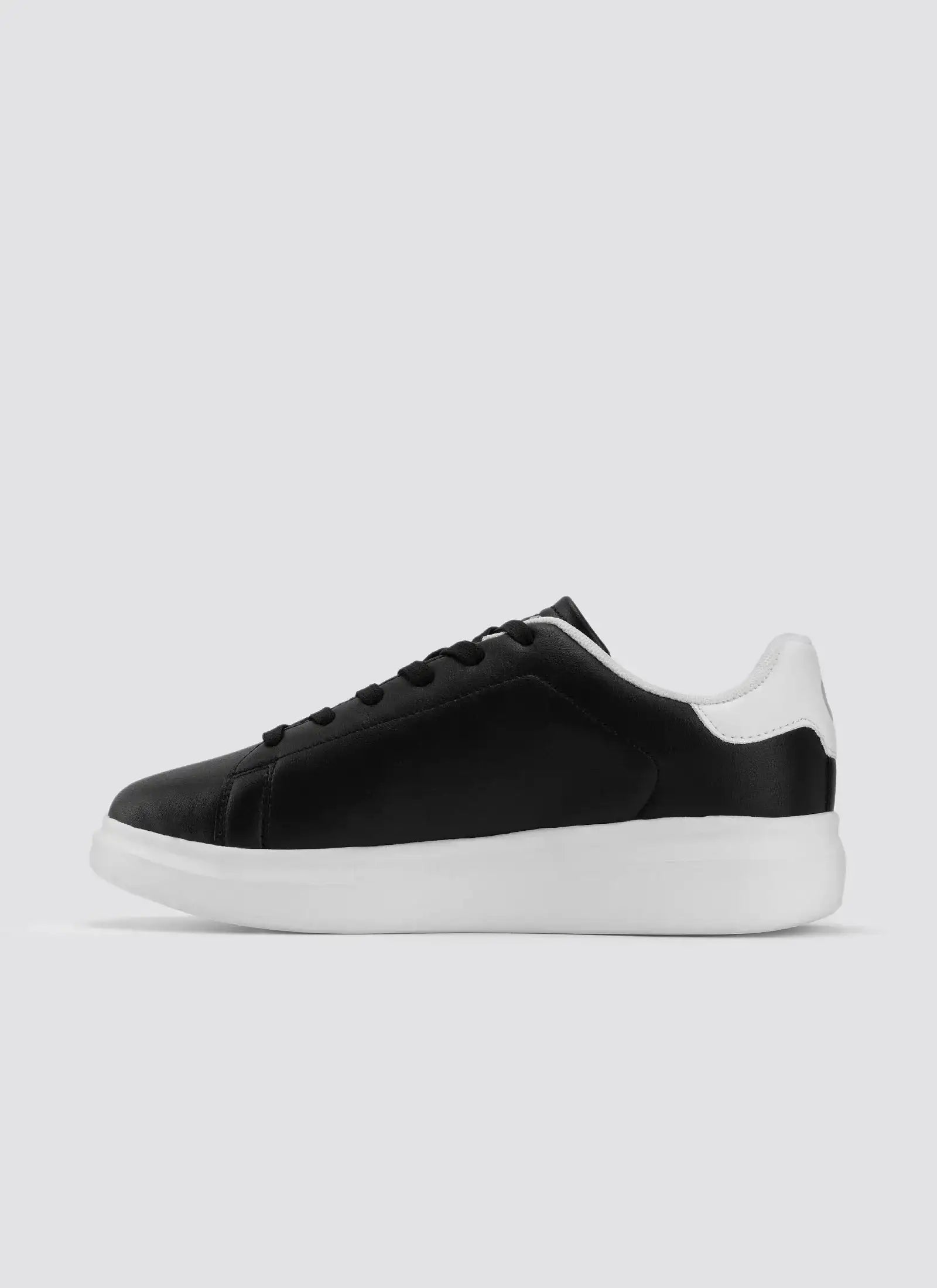 Black and white leather sneaker with white sole, side view on plain background