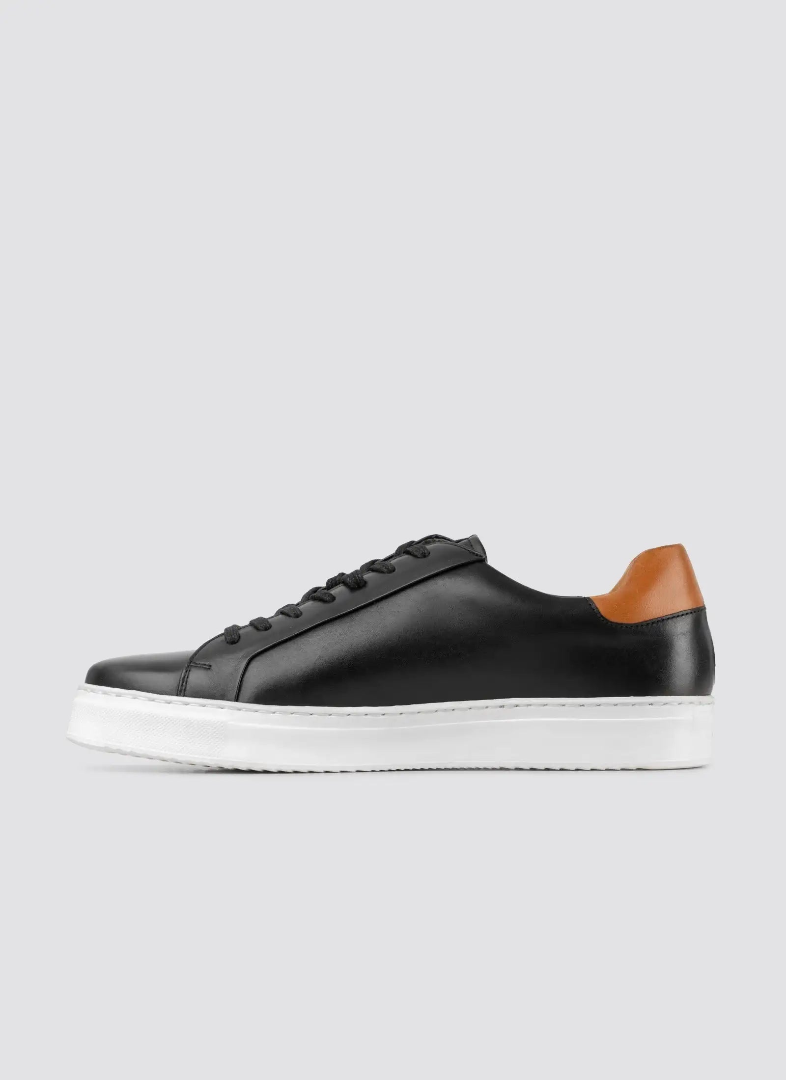 Black leather sneaker with brown accents on a light gray background