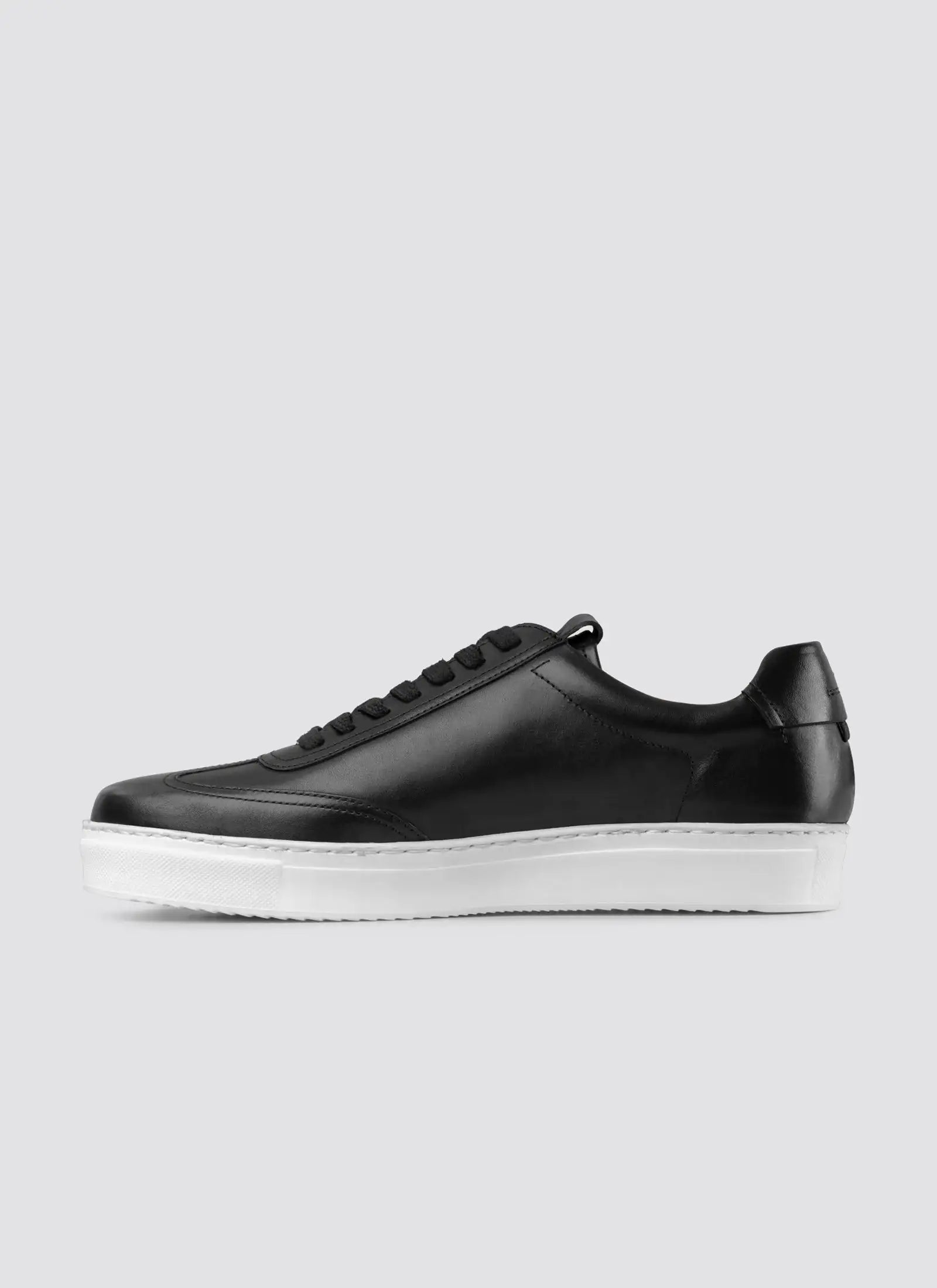 Black leather sneaker for men with white rubber sole, side view on grey background