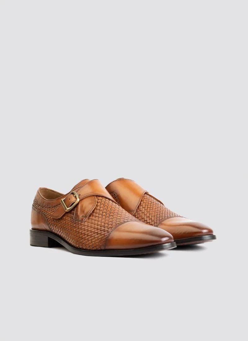 Tan leather monk strap shoes for men with woven texture and buckle detail on a plain background