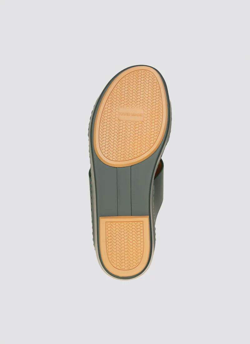 Close-up of men's shoe sole with textured rubber grip and olive green edging on a light background