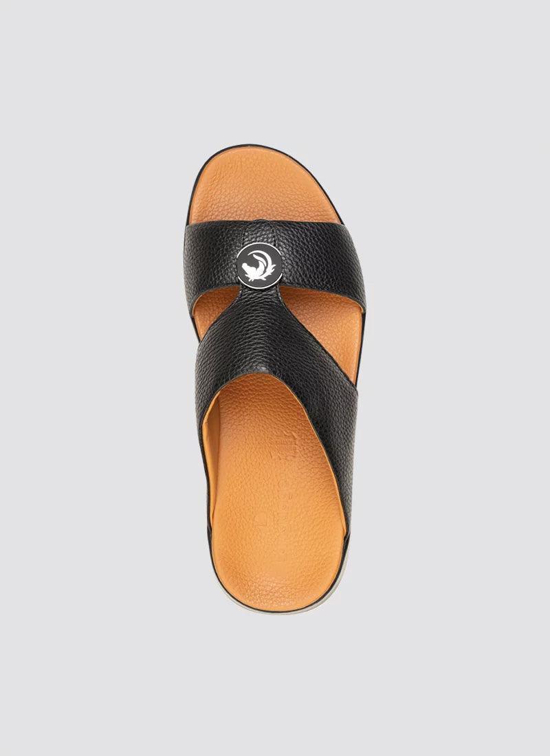 Men's black leather cross-strap sandal with tan sole and round metal accent, top view