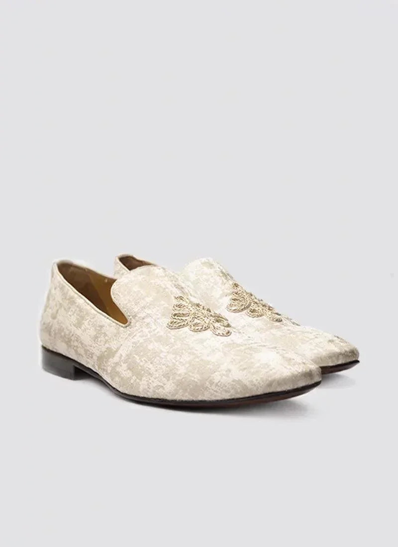 Beige slip-on loafers with embroidered detailing for men, placed on a plain background.