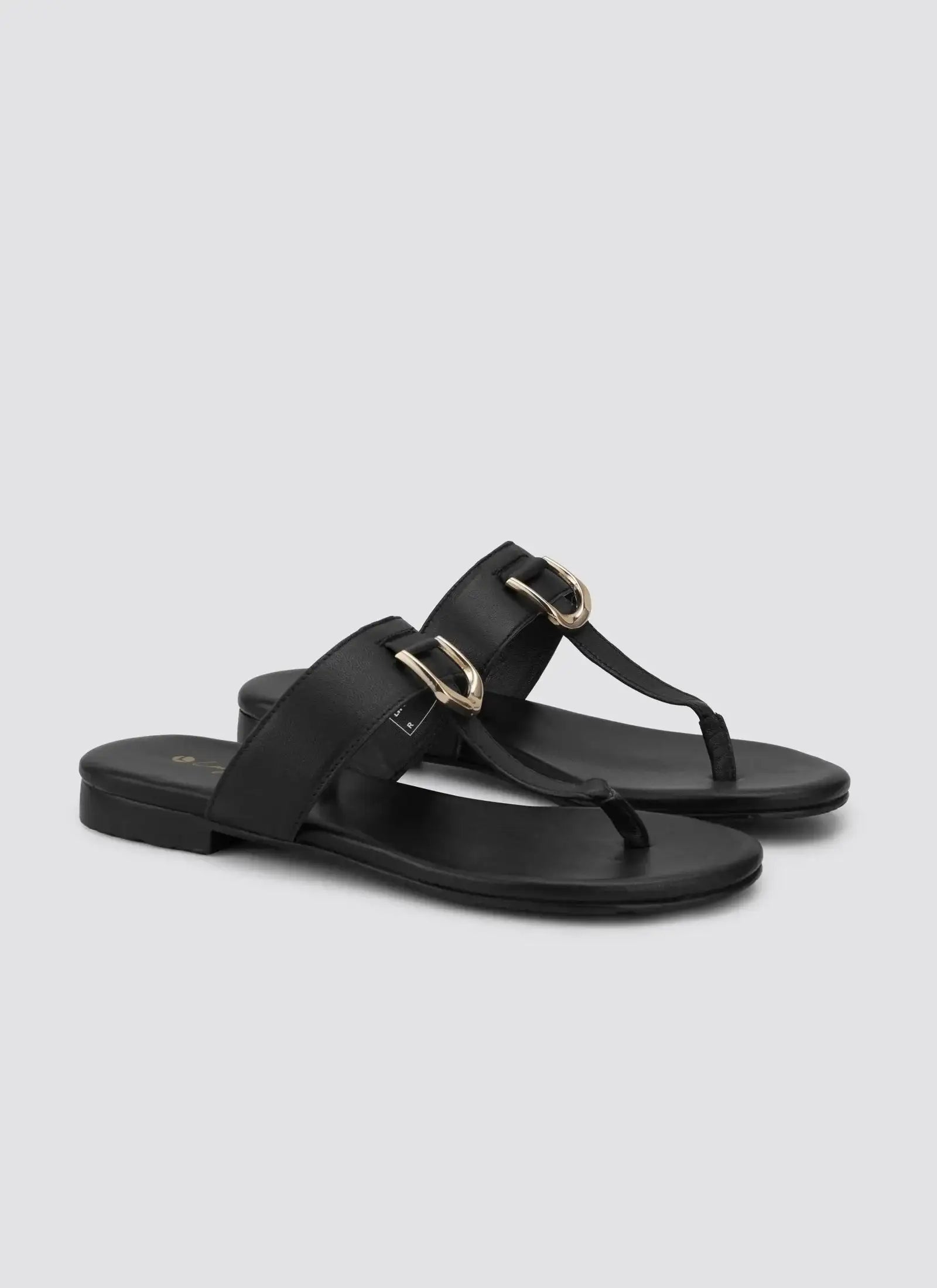 Black leather sandals with gold buckles and toe loop, flat sole, angled perspective