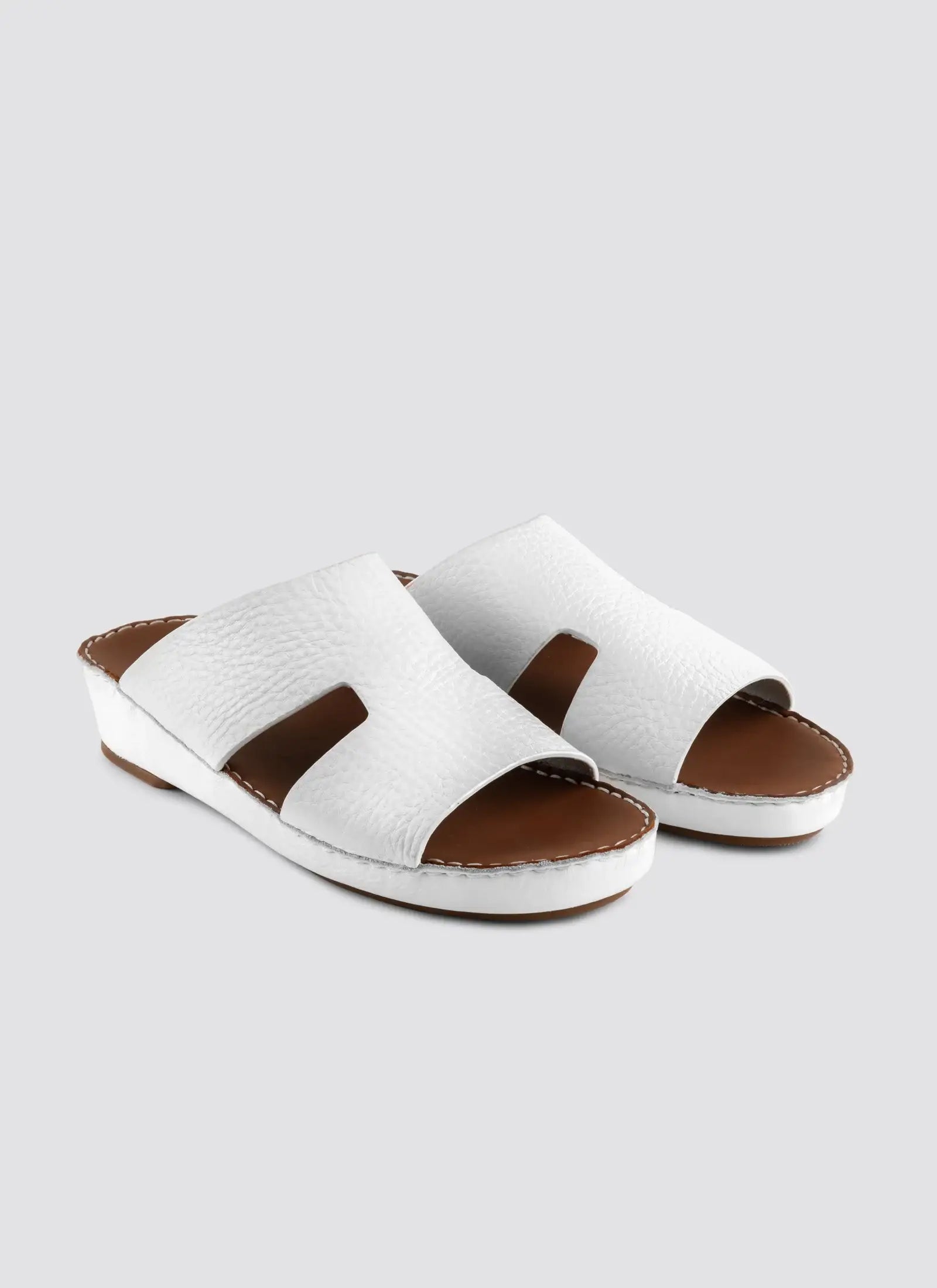 White sandals with brown accents on a light gray background #color_white