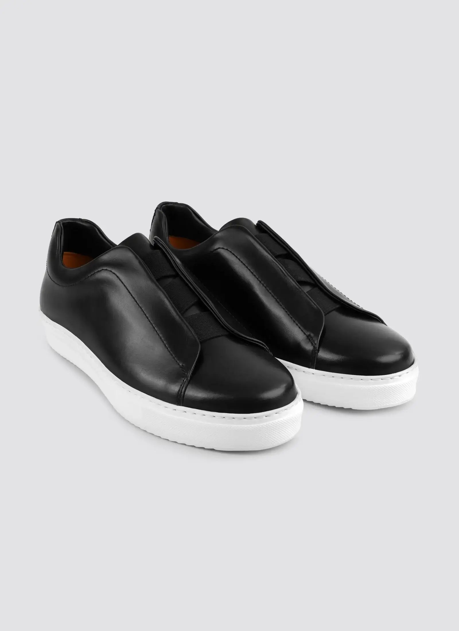 Black slip-on sneakers on a light gray background