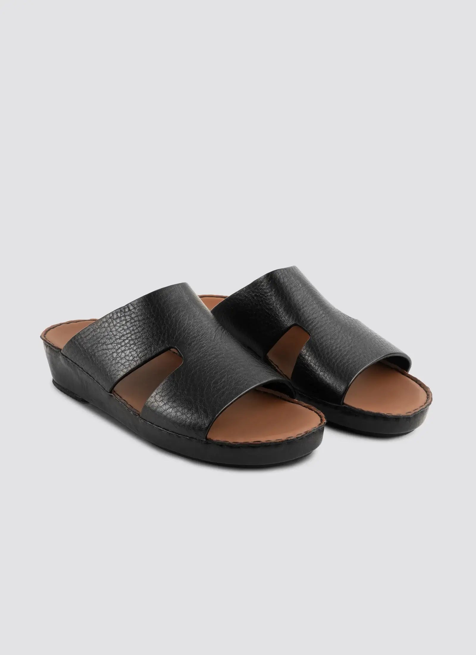 Pair of black sandals with brown soles on a light gray background