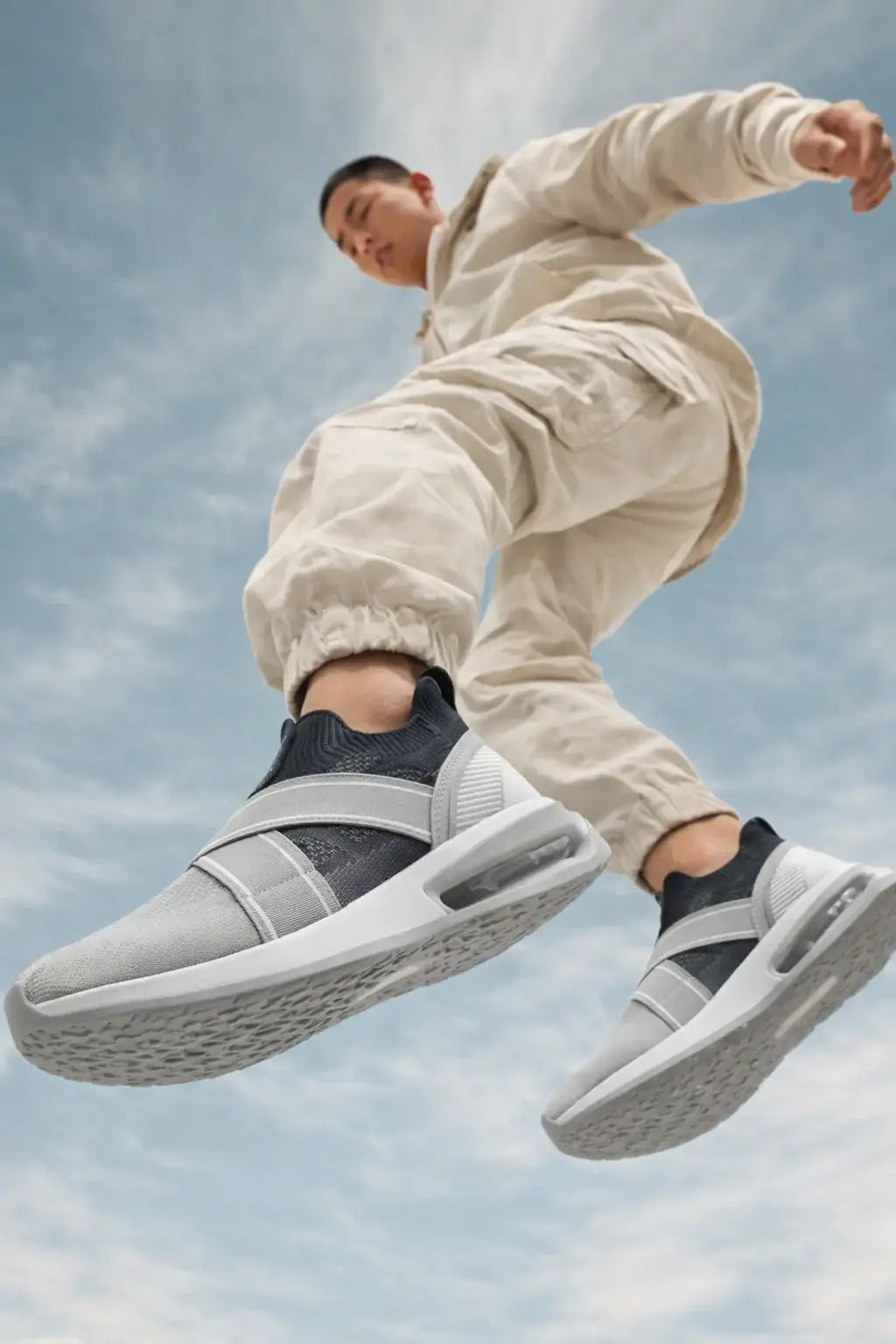 Man jumping in stylish grey and white slip-on sneakers against blue sky