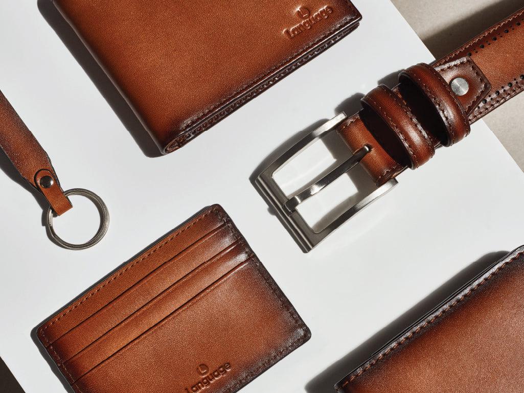 Brown leather wallet, card holder, belt, and keychain on a white background