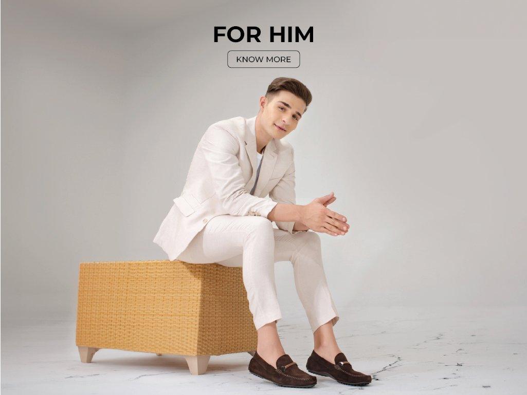 Man in cream suit wearing brown loafers, seated on light ottoman, men's footwear fashion