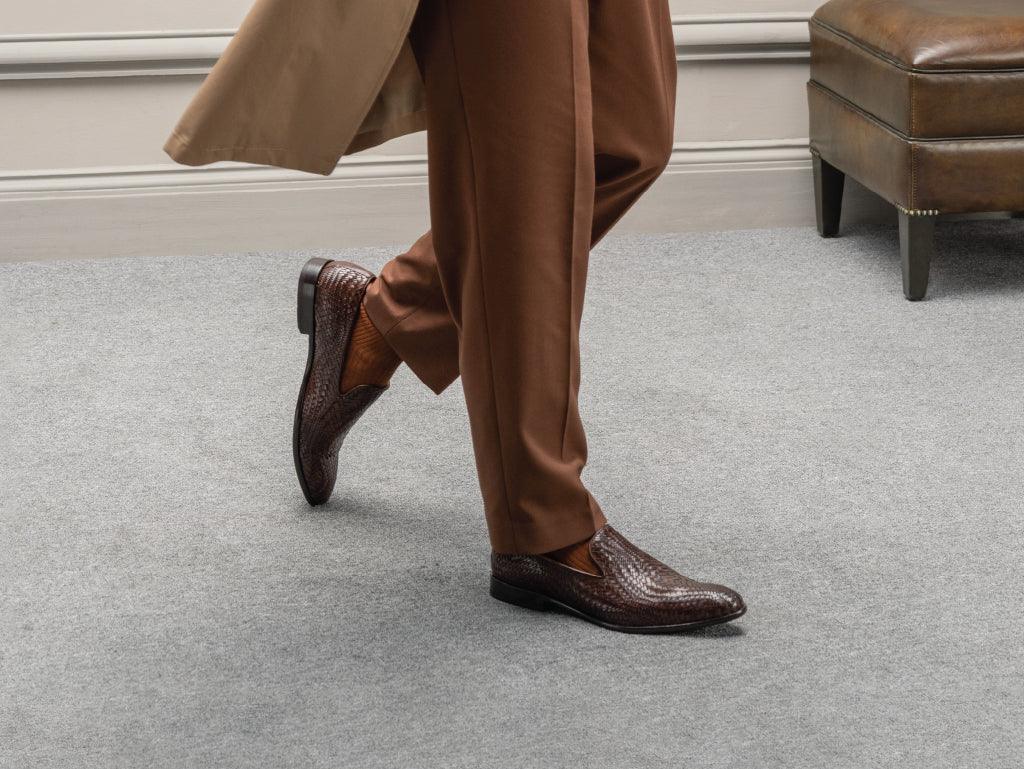 Men’s brown woven leather loafers paired with brown pants, styled in an elegant setting