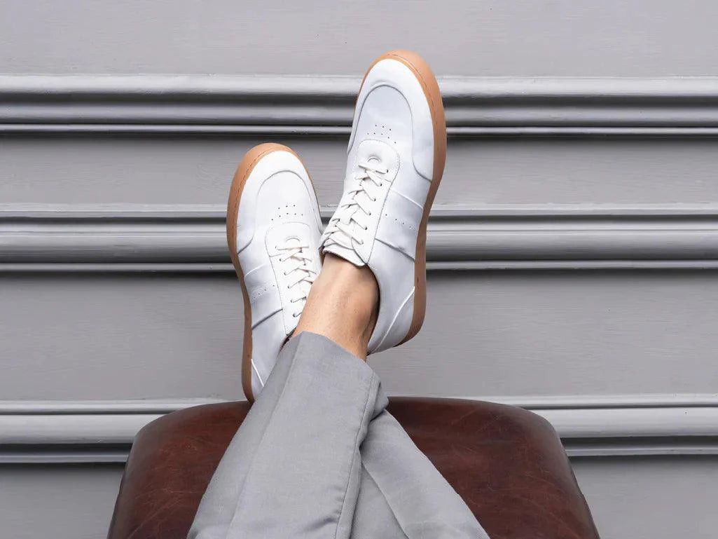 White leather sneakers with gum soles worn by person in grey pants, casual shoe style