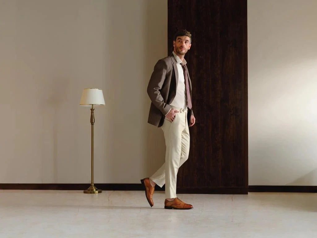 Man in formal attire wearing brown leather dress shoes, standing in a modern room
