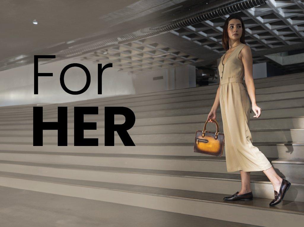 Woman in beige dress with brown leather handbag and black loafers walking down stairs