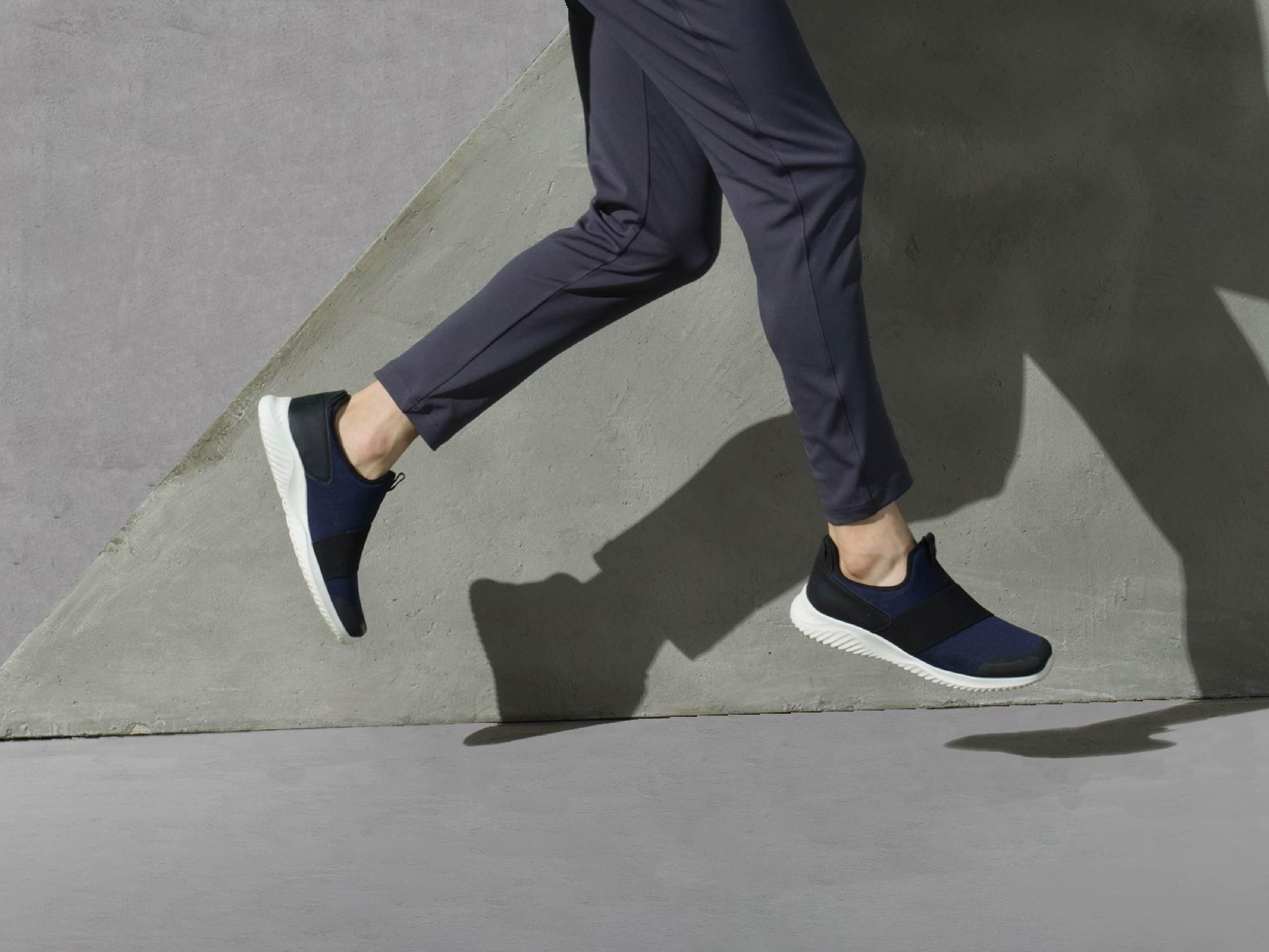 Man wearing navy blue slip-on sneakers with white soles jumping against a concrete wall