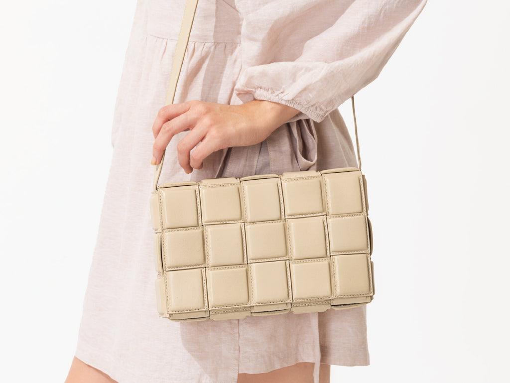 Woman holding a beige woven crossbody shoulder bag with geometric pattern