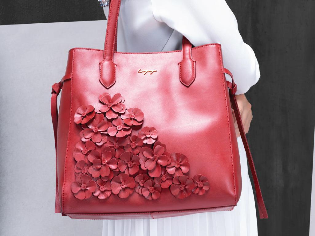 Red leather tote bag with 3D floral appliqué, held by a person in white outfit