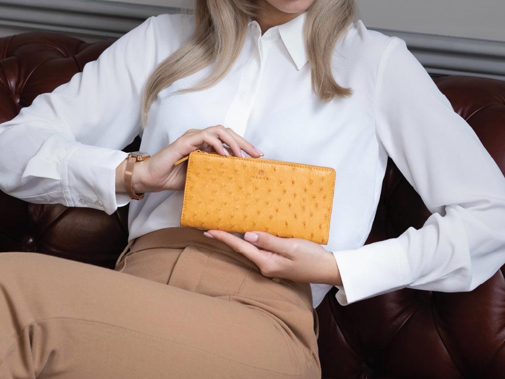 Woman holding yellow textured leather wallet, sitting on brown leather sofa