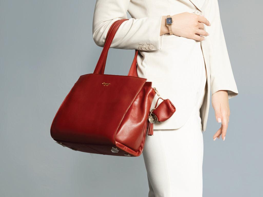 Woman in white suit holding a stylish red leather tote handbag with small pouch accessory