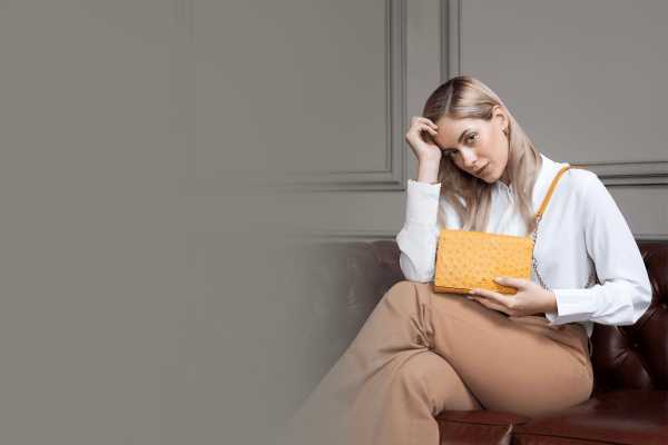 Woman sitting on leather sofa holding yellow handbag, stylish women's bag fashion