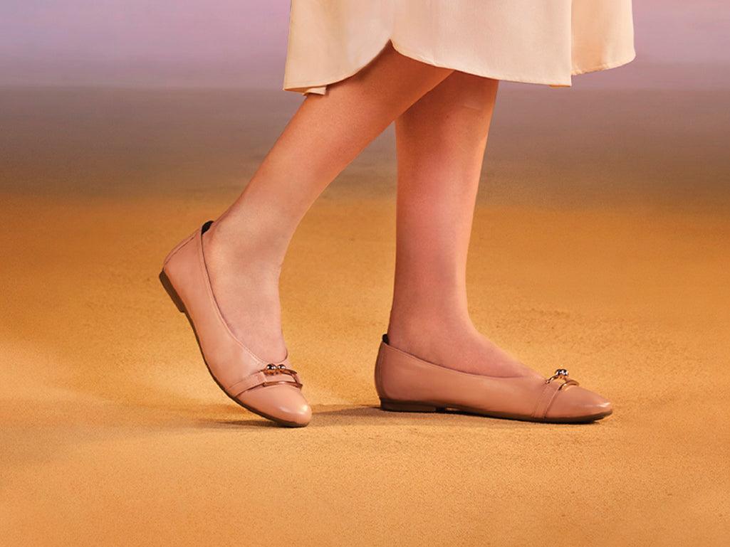 Woman wearing nude beige flat ballerina shoes on a sandy surface, elegant footwear
