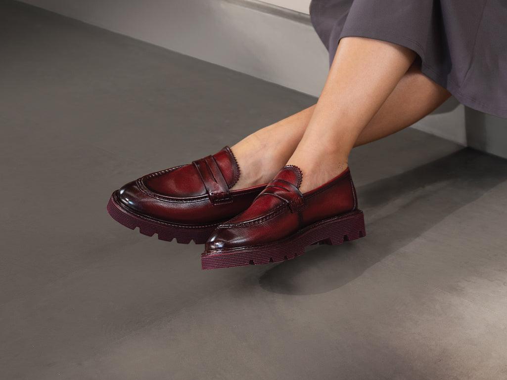 Women's feet wearing burgundy leather loafers with chunky soles on a smooth floor