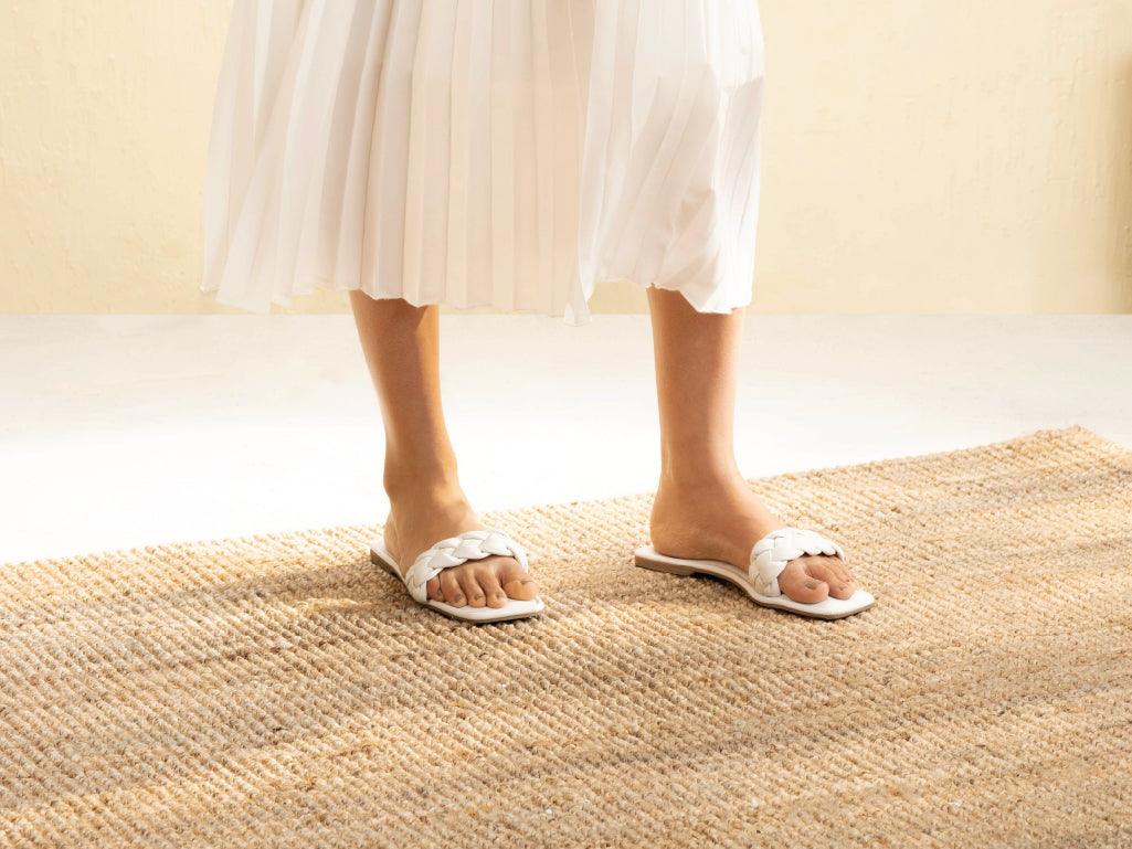 Woman wearing white braided slip-on sandals and pleated skirt on woven rug