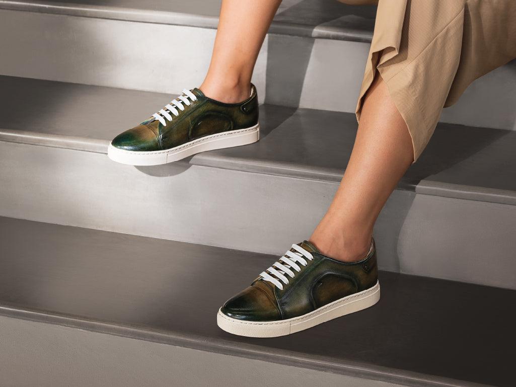 Woman wearing green leather sneakers with white soles sitting on gray stairs