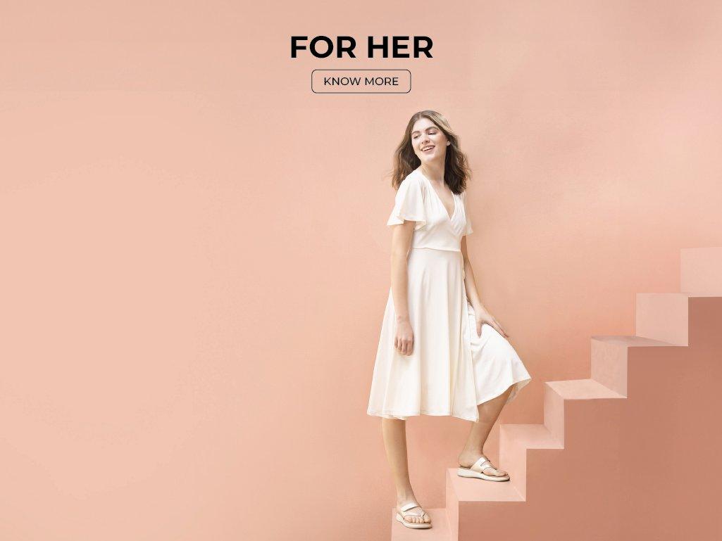 Woman in white dress wearing beige sandals, standing on pastel pink stairs, women's footwear fashion