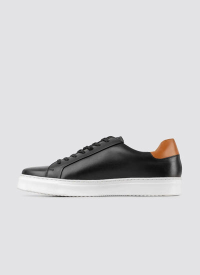 Black leather sneaker with brown accents on a light gray background 