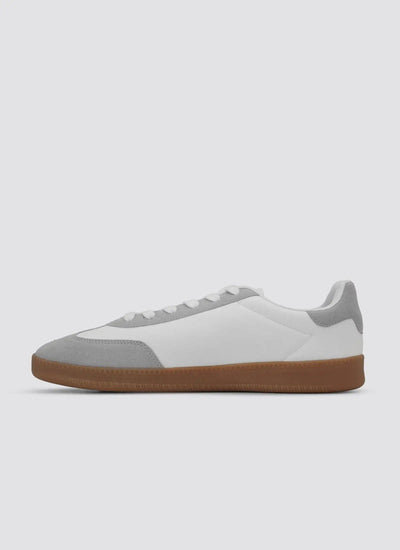 White and grey low-top sneaker with suede accents and brown rubber sole on plain background  