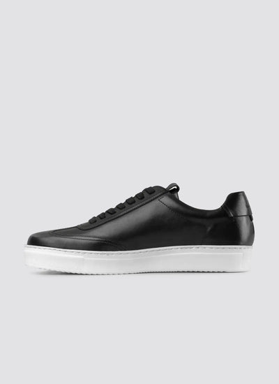 Black leather sneaker for men with white rubber sole, side view on grey background 