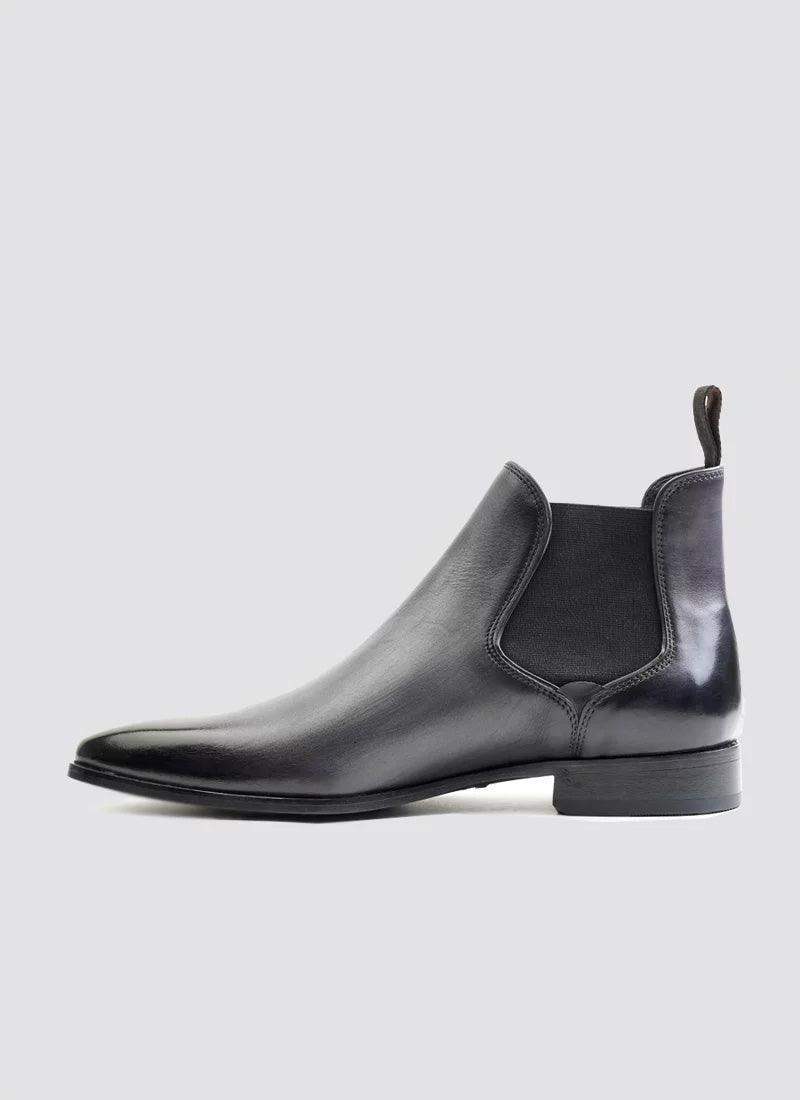 Men's black leather Chelsea boot with elastic side panel and pull tab on a plain background 