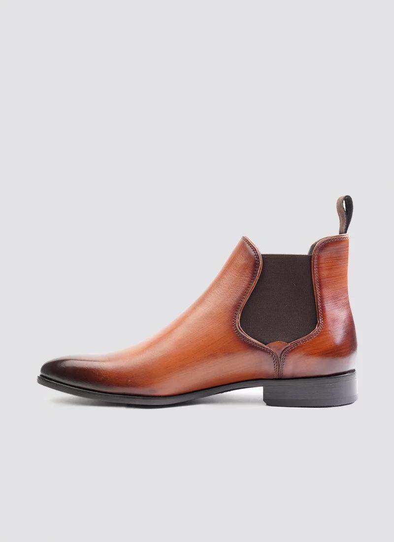 Tan leather Chelsea boot with elastic side panel, low heel, and pull tab on gray background 