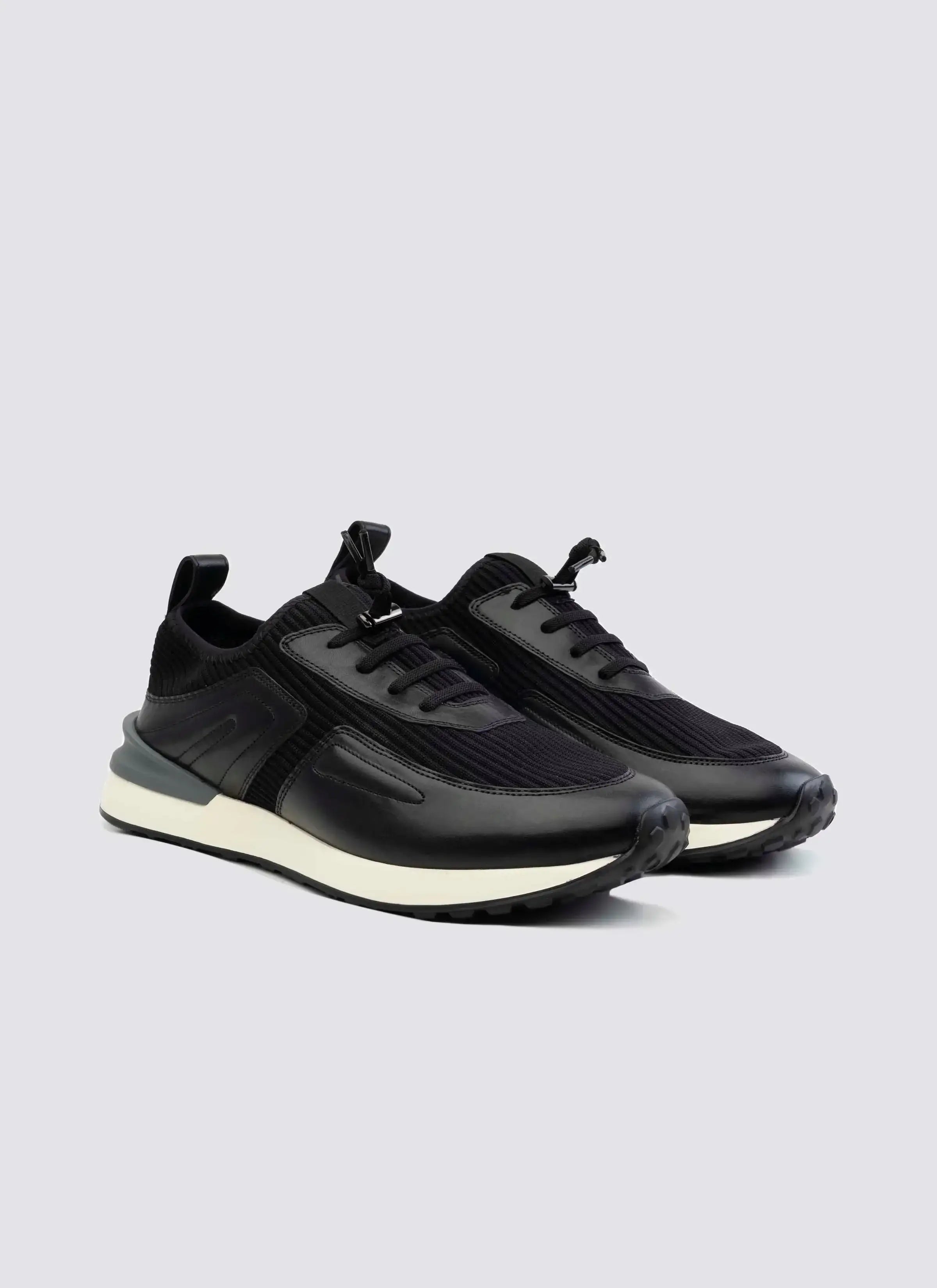Black low-top sneakers with white soles, lace-up design, and textured upper on a light background #color_black