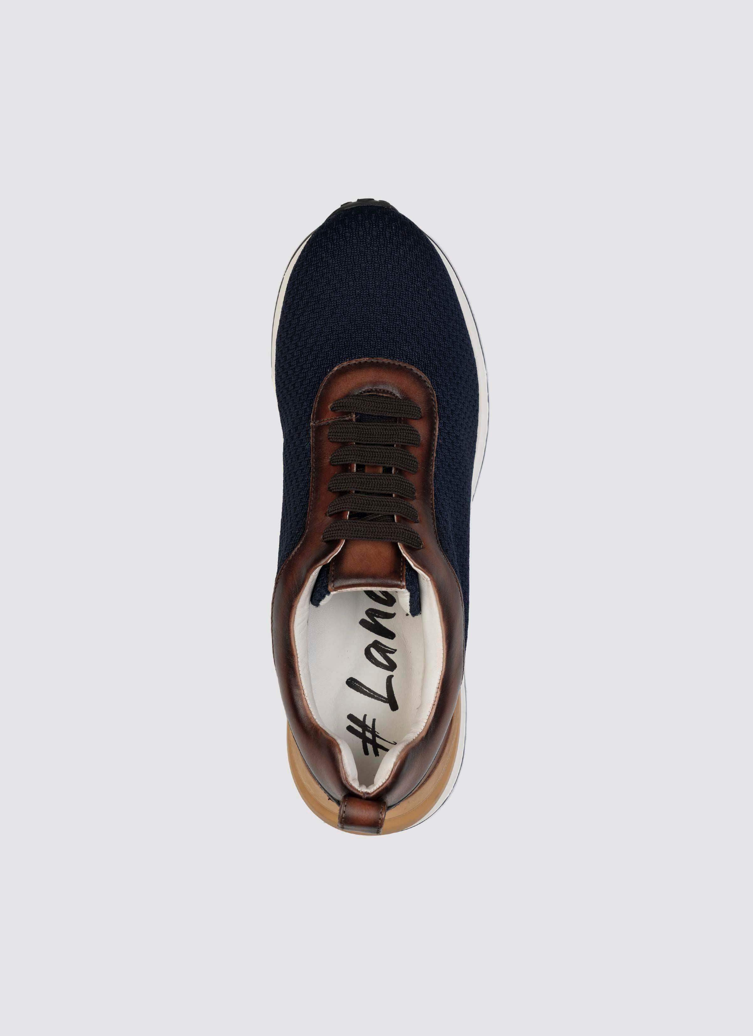 Top view of a navy blue sneaker with brown leather accents, white sole, and black laces. 