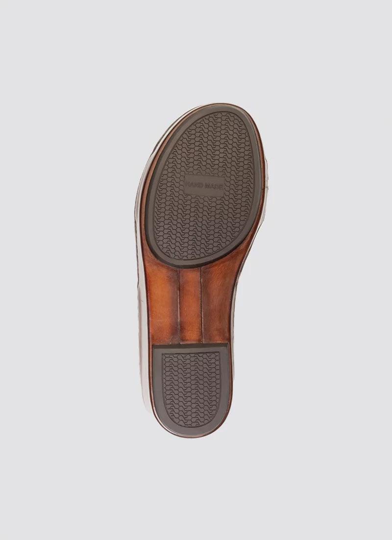 Brown leather shoe sole with textured rubber grip and handmade label, isolated on grey background.