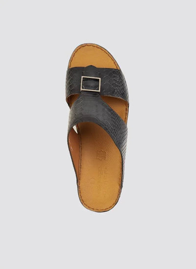 Men's black textured leather slide sandal with cross straps and silver buckle on tan footbed