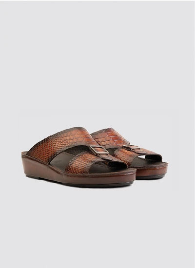 Brown slip-on sandals with textured pattern, metal buckles, and low wedge sole on gray background