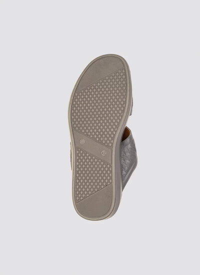 Close-up of the textured rubber sole of a grey woven slip-on shoe on a plain background 