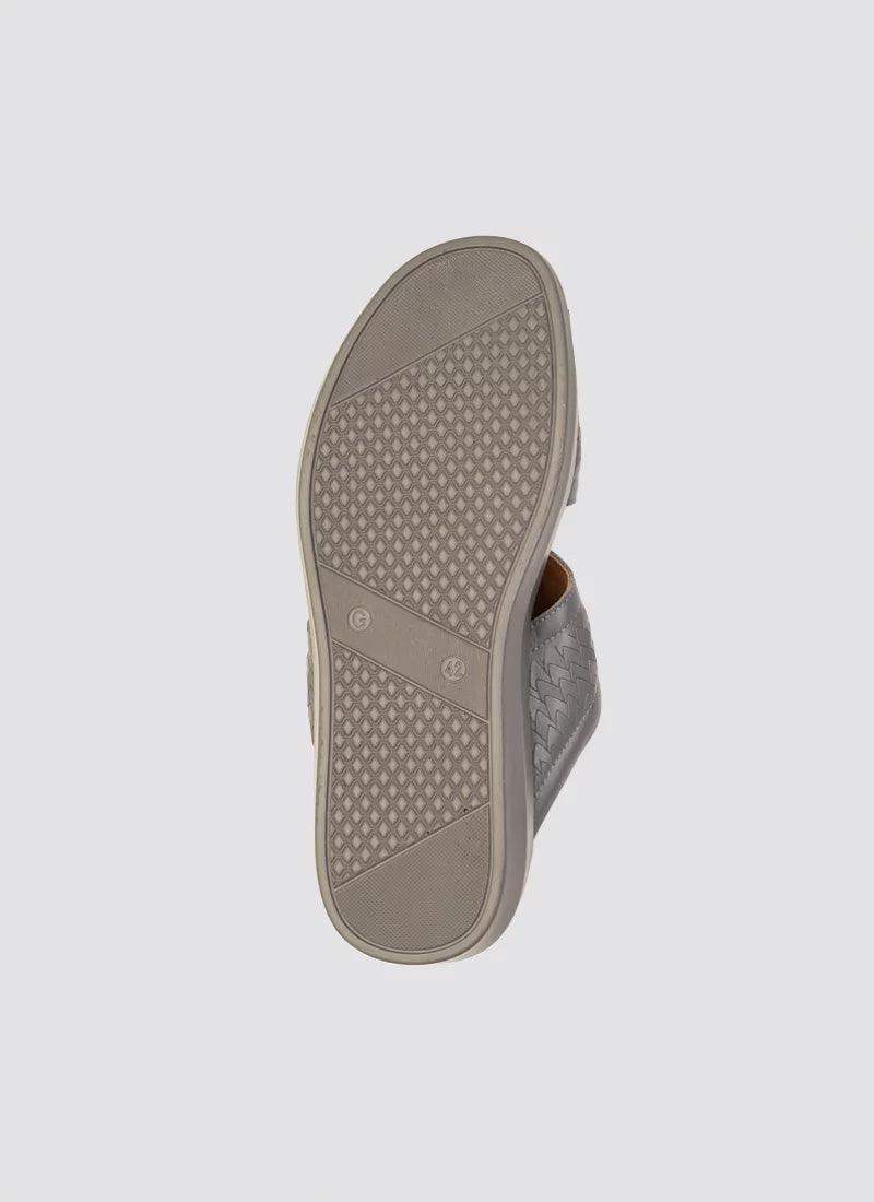 Close-up of the textured rubber sole of a grey woven slip-on shoe on a plain background 