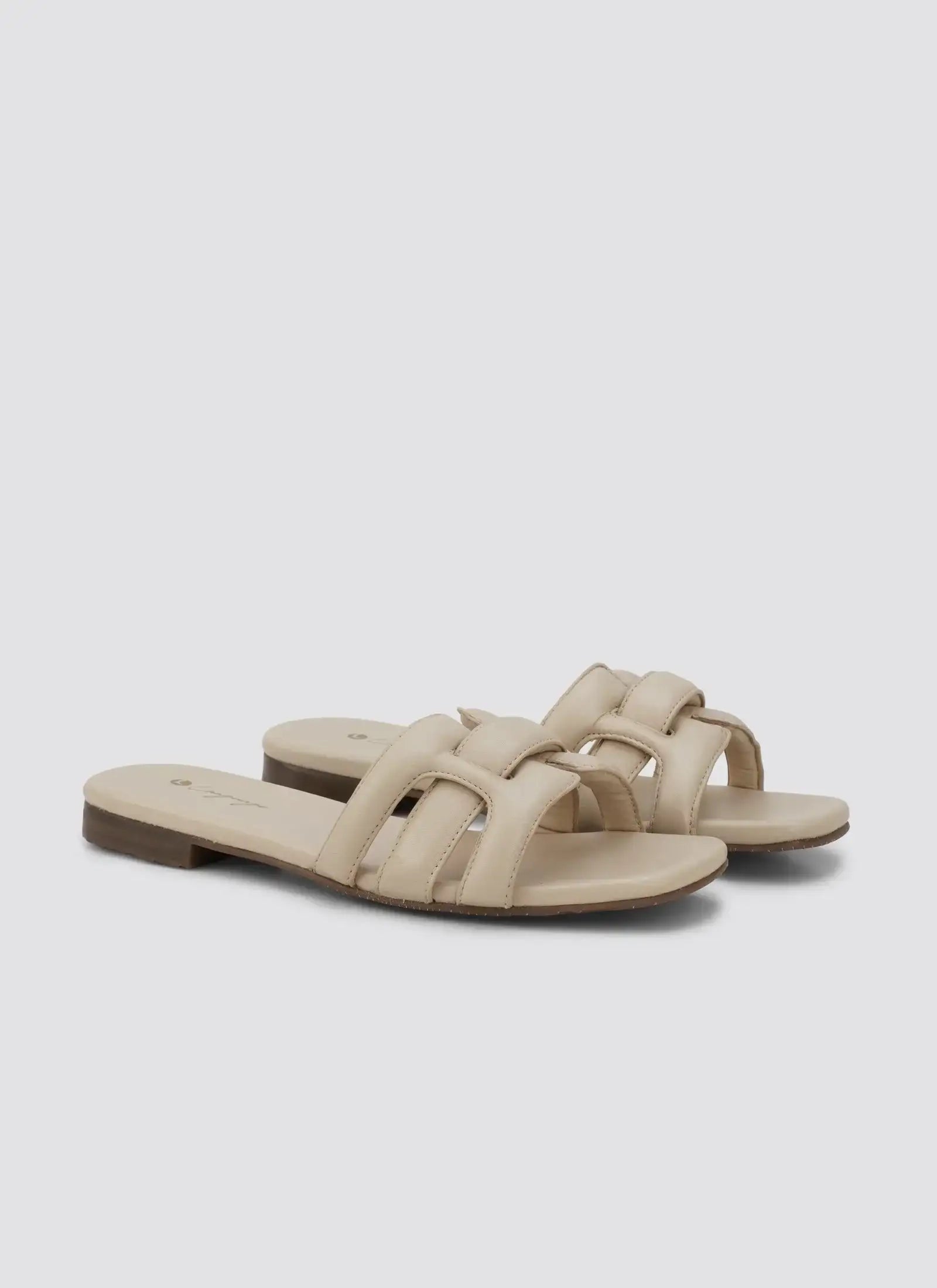 Pair of nude beige flat leather slide sandals with padded straps on a white background  