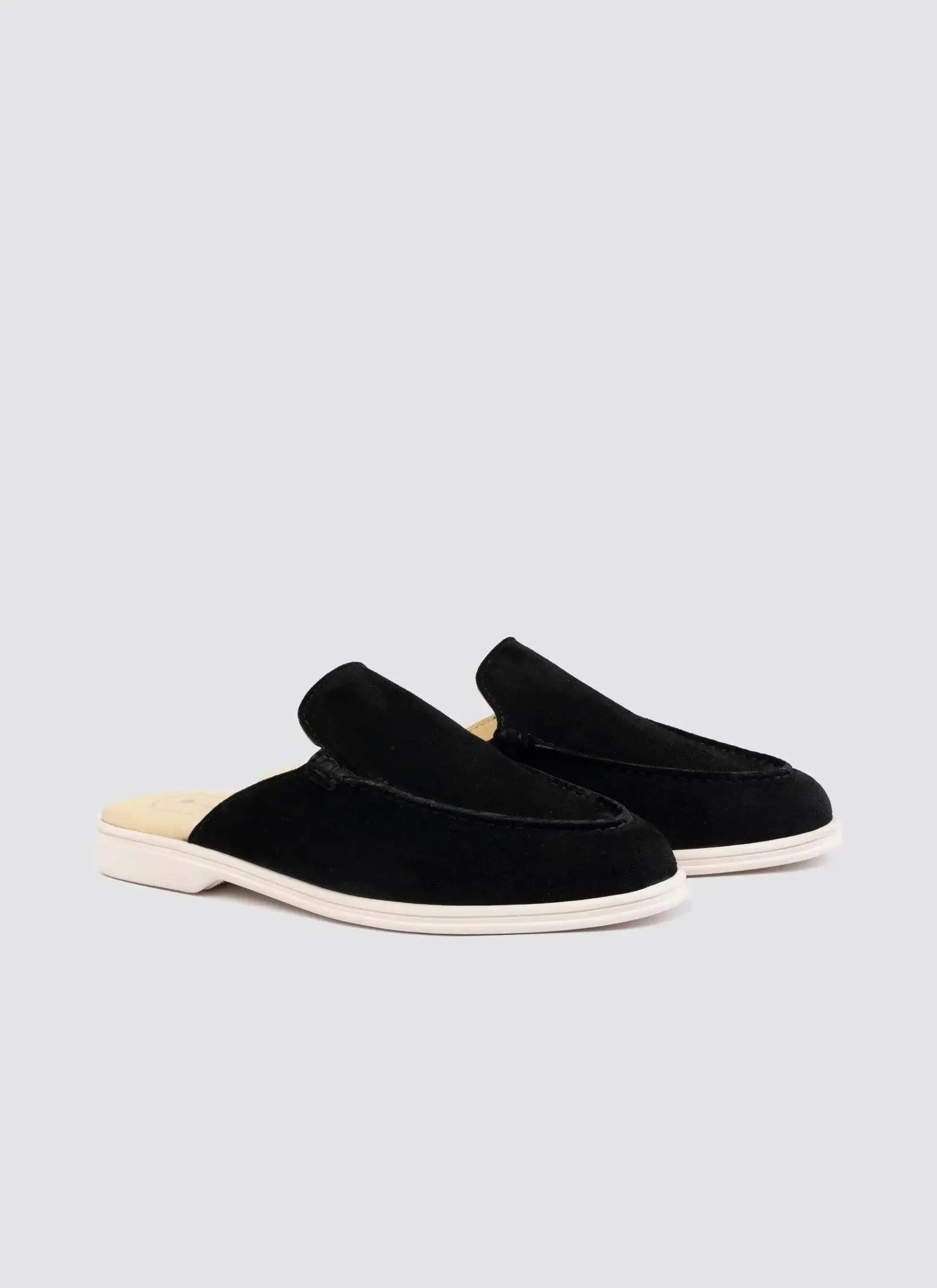 Black suede slip-on loafers with white soles on a plain background 