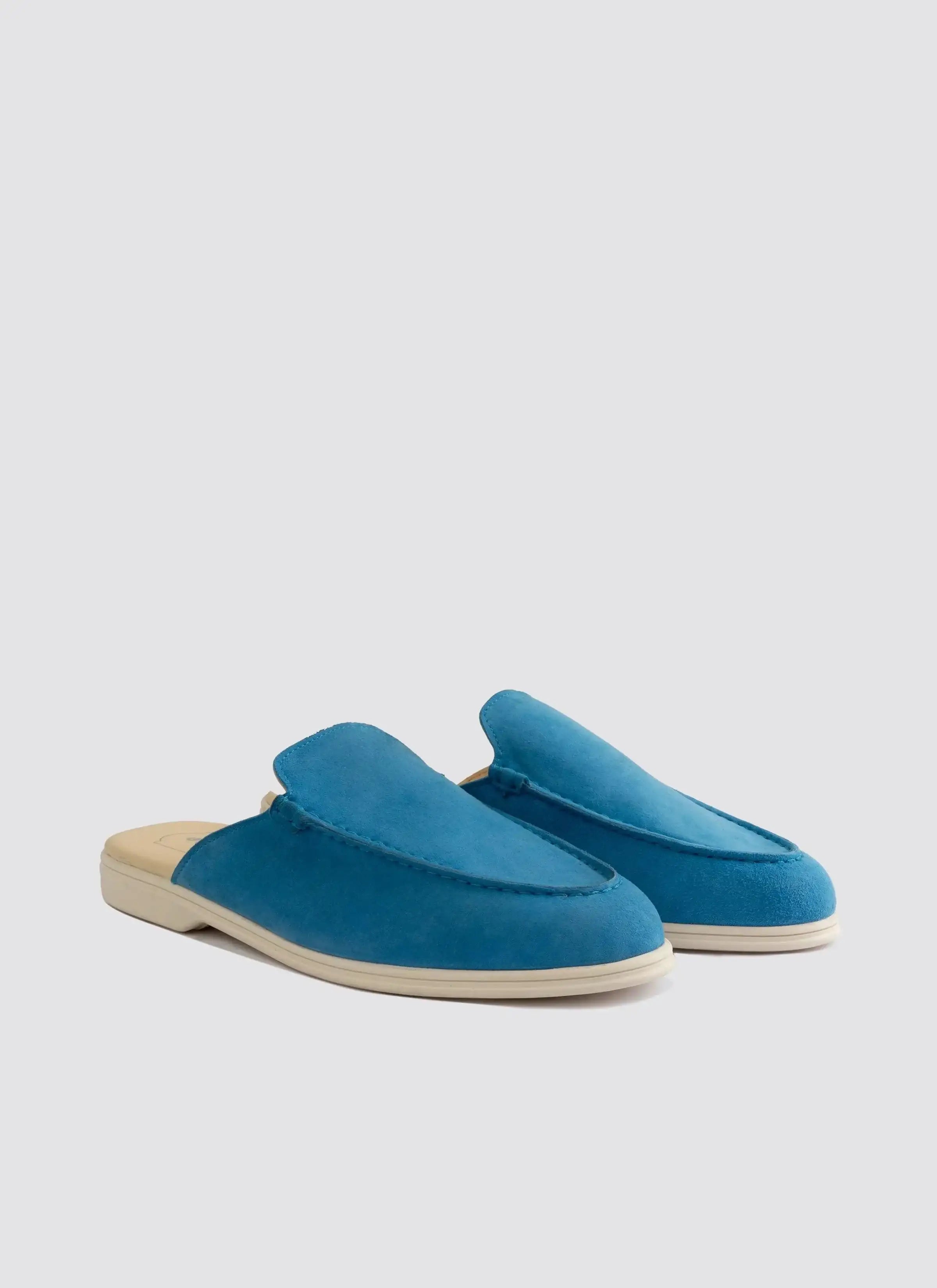 Pair of blue suede slip-on loafers with beige soles on a plain background 
