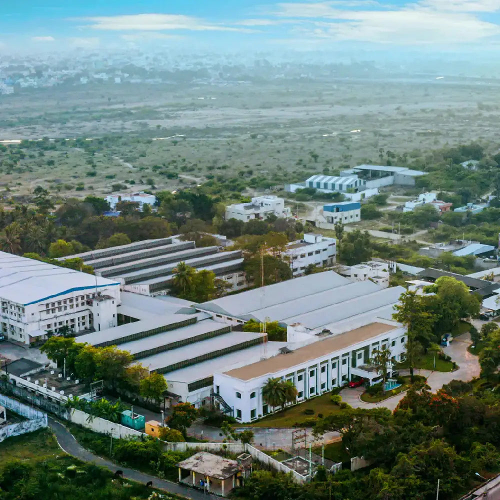 Aerial view of a footwear and bag manufacturing facility with multiple white buildings and greenery