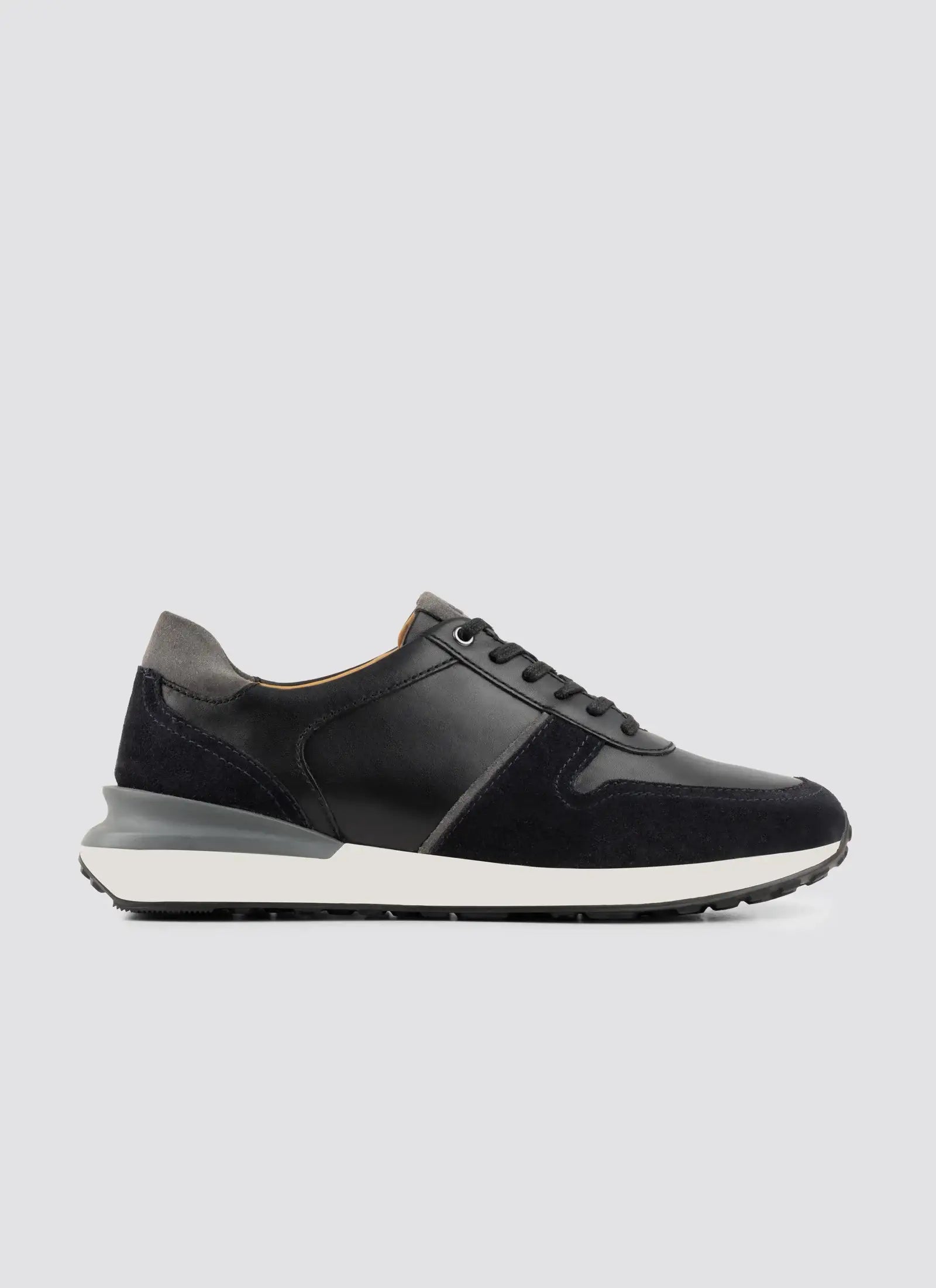 Men's black leather and suede sneaker with white sole, side profile on plain background  