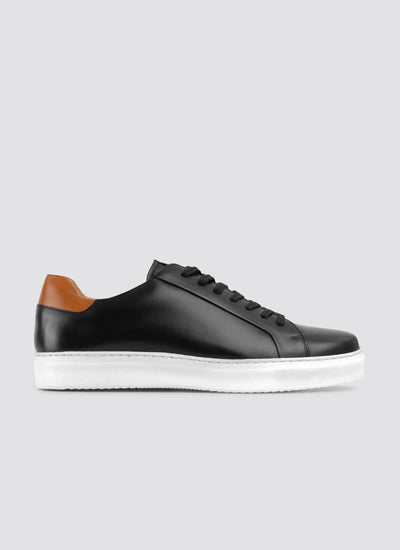Black leather sneaker with brown accents on a light gray background 