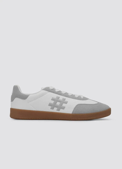 White and grey low-top sneaker with gum sole, suede accents, and hashtag design on side 