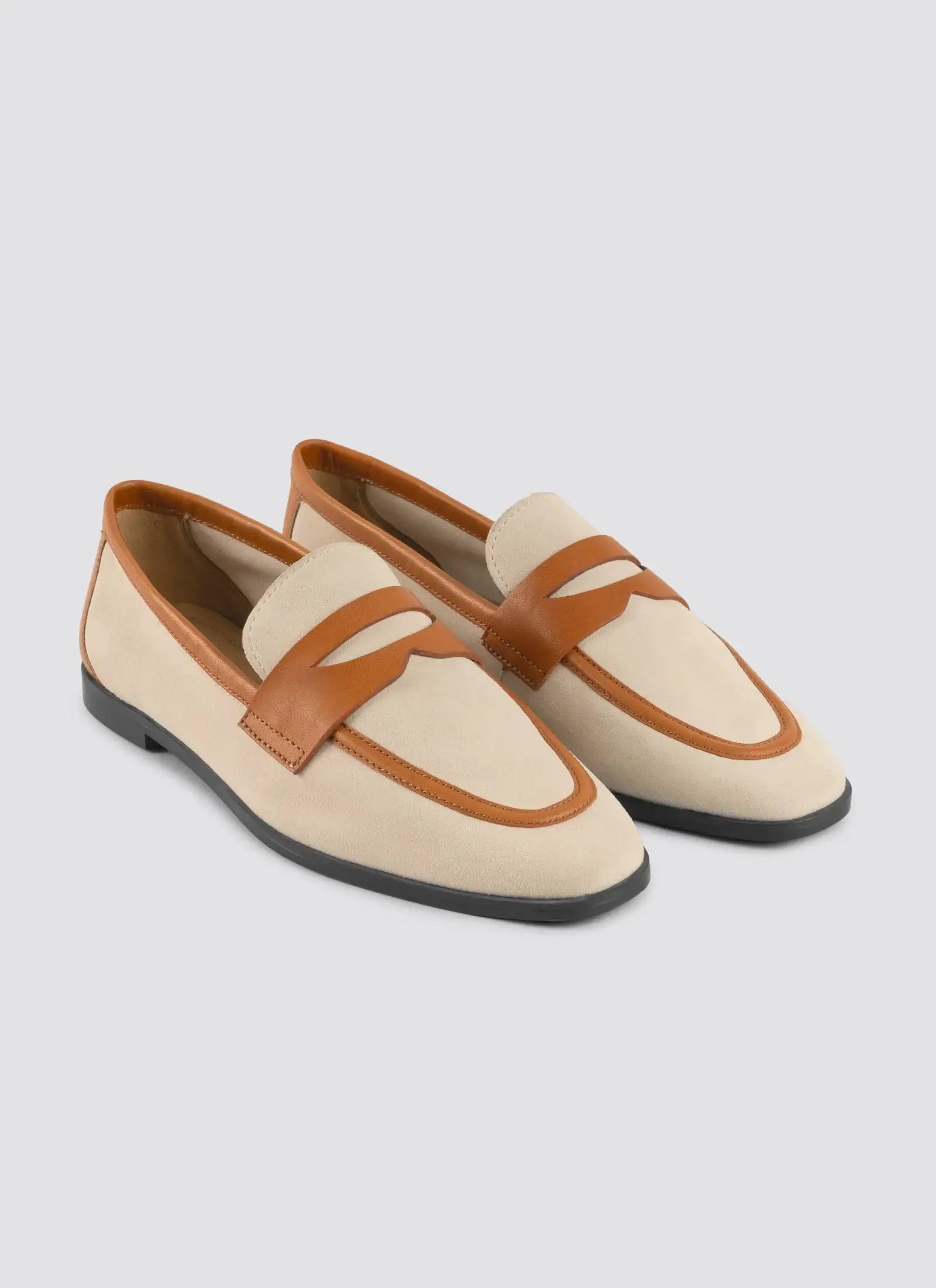 Pair of beige loafers with brown straps on a light gray background 